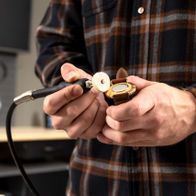 Ein Mann hält den flexiblen Wellenanschluss des Doppelschleifers HG35 von Scheppach in der Hand. Der Anschluss ist mit einer Schleifscheibe verbunden.