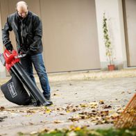 Ein Mann bedient den Laubsauger und -bläser BBV500-40Li von Scheppach auf einer Betonfläche mit Laub.