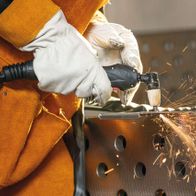 Ein Arbeiter verwendet das Scheppach 3in1 Kombi-Schweißgerät WSE4000-CUT zum Plasmaschneiden. Funken fliegen von der Schneidstelle weg. Der Arbeiter trägt Schutzhandschuhe und eine Schutzbrille.