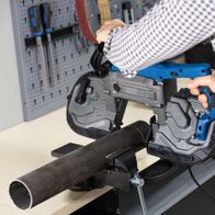 Metallbandsäge MBS1200xt von Scheppach im Einsatz. Eine Person bedient die Säge, die ein Metallrohr schneidet. Im Hintergrund sind Werkzeuge an der Wand befestigt.