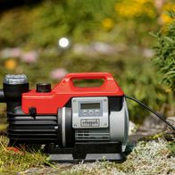 Hauswasserautomat GP1000 Jet LCD Scheppach, seitlich fotografiert. Im Hintergrund ist ein Garten mit Pflanzen zu sehen.