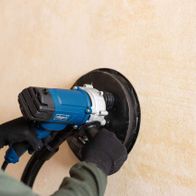 Wand- und Deckenschleifer DS200 von Scheppach im Einsatz. Die Maschine wird von einer Person an einer Wand verwendet. Der Schleifteller ist aktiv und berührt die Wand.