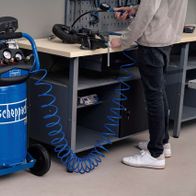 Scheppach Kompressor HC80V mit blauer Schlauchrolle und Werkbank. Ein Mann bedient den Kompressor.