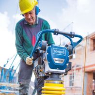 Ein Arbeiter bedient den Vibrationsstampfer VS1000 von Scheppach auf einer Baustelle. Der Stampfer hat 6,5 PS und ist im Einsatz zu sehen.