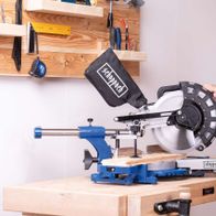 Ein Mann bedient eine Kappzugsäge von Scheppach. Die Säge ist auf einem Holztisch montiert und wird von dem Mann mit beiden Händen bedient. Im Hintergrund sind verschiedene Werkzeuge an der Wand befestigt.