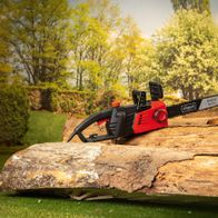 Elektro-Kettensäge CSE2700 von Scheppach auf einem Baumstamm im Garten. Die Säge liegt auf dem Holz und ist bereit für den Einsatz.