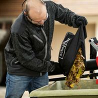 Ein Mann leert einen mit Laub gefüllten Beutel in einen Scheppach Laubsauger und -bläser. Der Laubsauger und -bläser BBV500-40Li von Scheppach ist auf einem Wagen montiert.