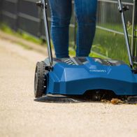 Scheppach Kehrmaschine Trike-S mit Fußgängeraufsatz, die eine Straße reinigt