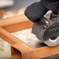 Siliziumkarbidbürste von Scheppach im Einsatz an einer MRS1300 Satiniermaschine. Die Bürste wird von einem blauen Elektrowerkzeug gehalten und bearbeitet ein Metallteil.