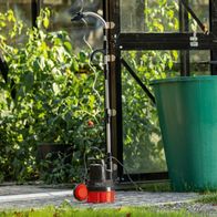 Scheppach Regenfasspumpe RBP350 mit Schlauch und Sprühdüse für 2-in-1-Funktion, in einer Gartenumgebung platziert