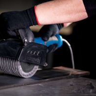 Gedrehte Metalldrahtbürste von Scheppach im Einsatz an einer Maschine. Die Bürste wird von einer Hand mit Schutzhandschuh gehalten.