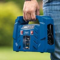 Ein Mann hält den tragbaren Kompressor Airforce 5 von Scheppach in der Hand. Der Kompressor hat ein LCD-Display und verschiedene Anschlüsse. Das Gerät ist blau und hat einen Handgriff oben.