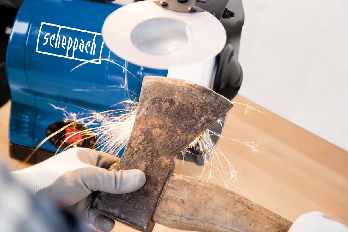 Ein Scheppach Doppelschleifer BG200AL wird zum Schleifen eines Holzstücks verwendet. Ein Handschuh ist sichtbar.