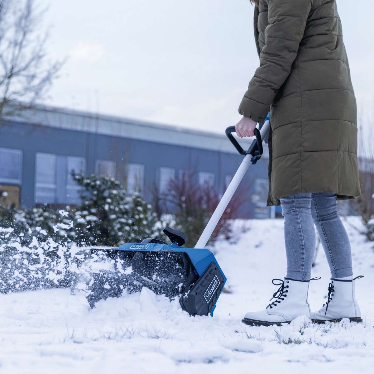 Person beim Schneefräsen mit Scheppach-Akku-Schneefräse, Blick auf die Arbeitsbreite und Schneefräse-Ablenkung.