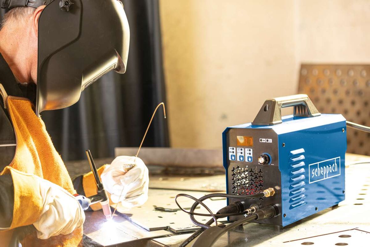 Ein Arbeiter schweißt mit dem Schweißgerät WIG1000-Multi von Scheppach. Das Gerät liegt auf einem Tisch und ist angeschaltet. Der Arbeiter trägt eine Schweißerbrille und einen Schweißerschutz.