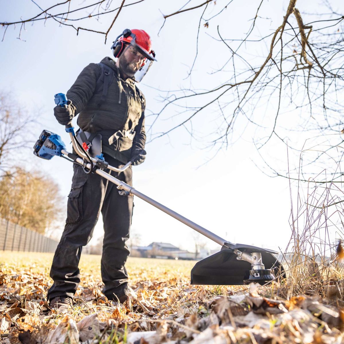 Mann mit Akku-Freischneider beim Einsatz im Garten, mit Sicherheitsausrüstung und Werkzeug