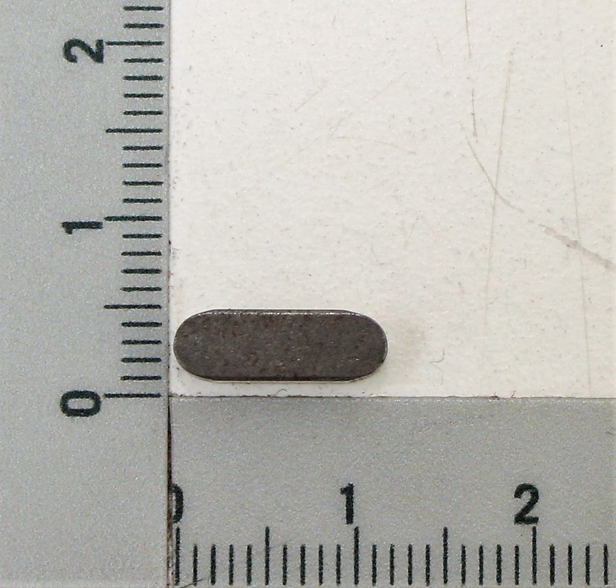 Passfeder A4x4x12 neben einer Skala zur Größenveranschaulichung. Die Passfeder liegt horizontal auf der Skala.