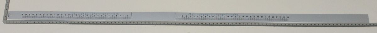 Eine lange Metalllineal mit Zentimeter- und Millimeterangaben, von vorne fotografiert.