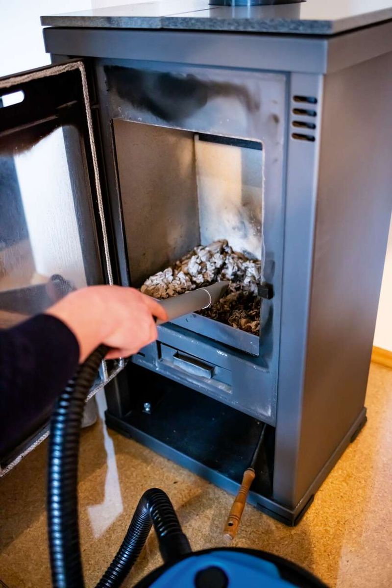 Der Aschesauger AVC20 von Scheppach im Einsatz. Eine Hand hält den Schlauch, während Asche aus einem Ofen entfernt wird. Der 20L Behälter und der feuerfeste Schlauch sind sichtbar.