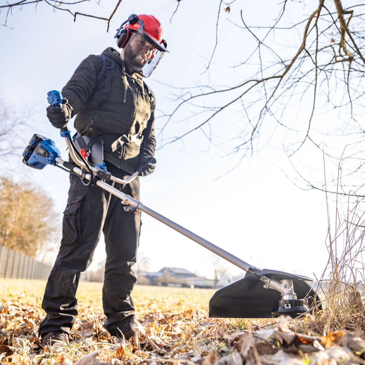 Mann mit Akku-Freischneider beim Einsatz, Schultergurt und Werkzeug in Einsatzposition