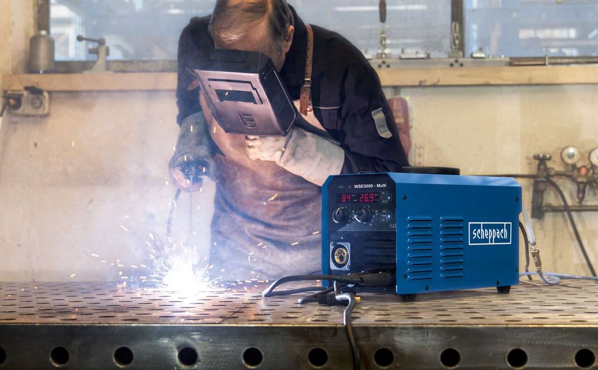 Ein Arbeiter schweißt mit dem Schweißgerät Fülldraht WSE5000-Multi von Scheppach. Das Gerät liegt auf einem Metalltisch und zeigt 84% und 269° an.