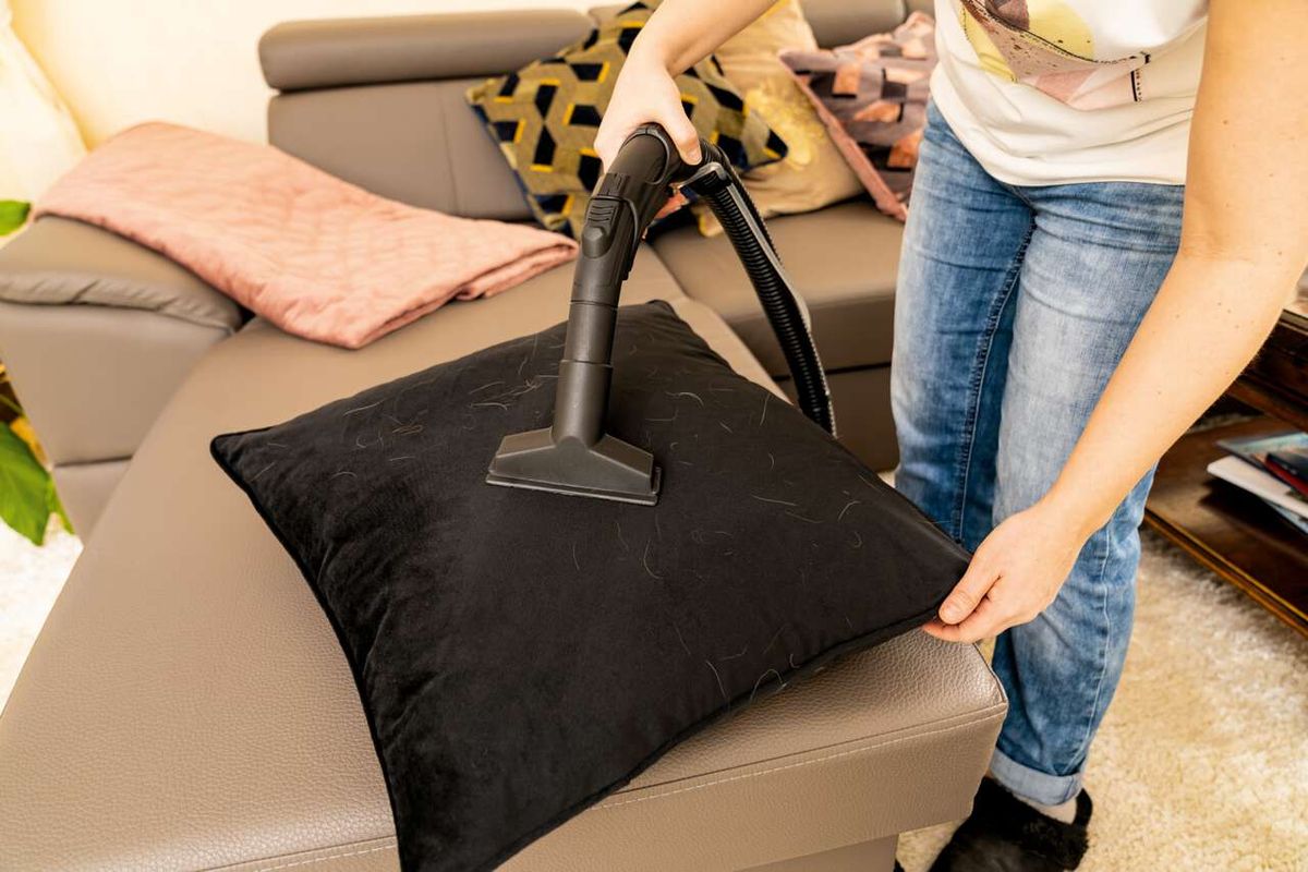 Eine Person reinigt ein Sofa mit dem Scheppach SprayVac20. Der schwarze Aufsatz liegt auf einem Kissen. Der Sauger ist an der schwarzen Düse befestigt.