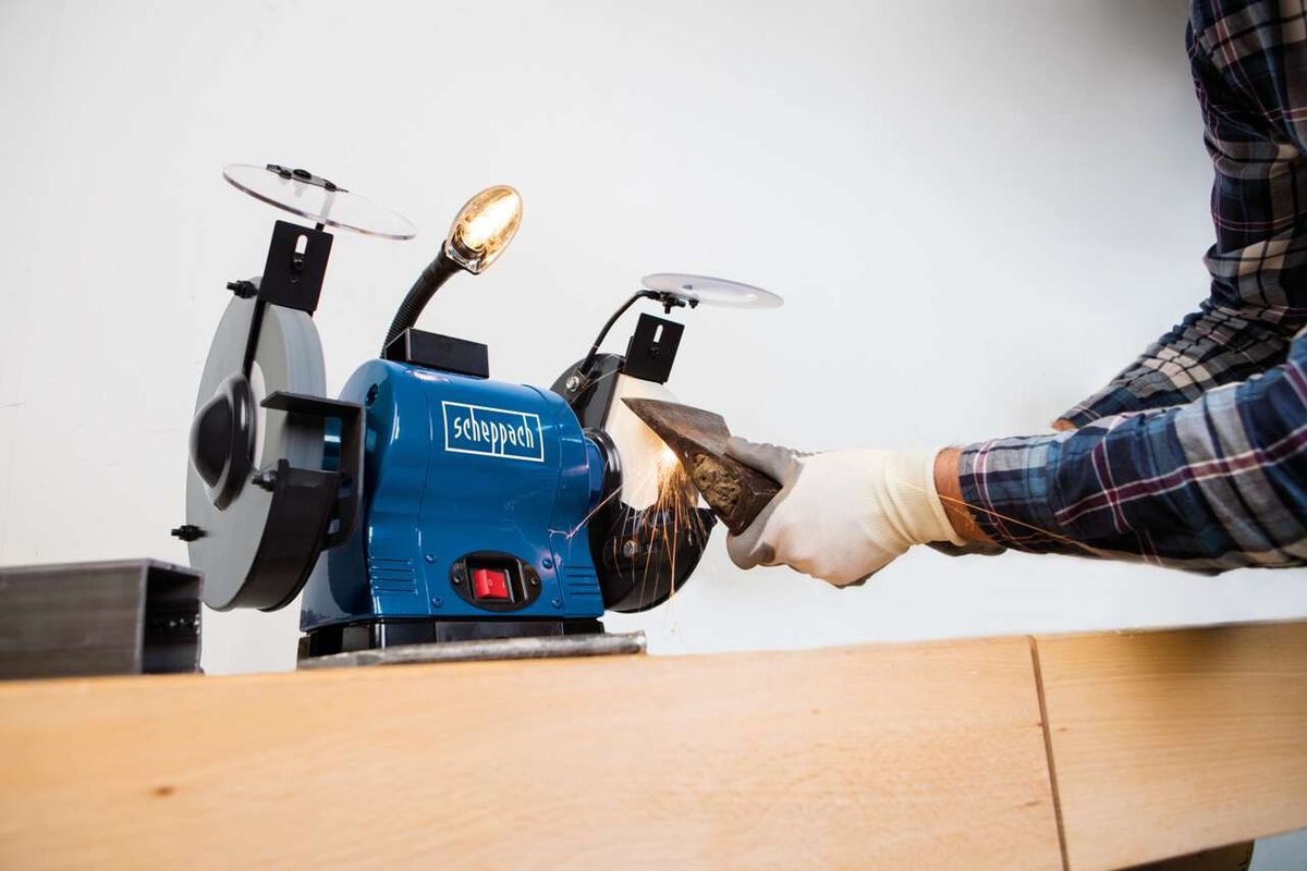Scheppach Doppelschleifer BG200AL im Einsatz. Ein Handschuh schützt die Hand beim Schleifen. Die Maschine wird von oben gezeigt.