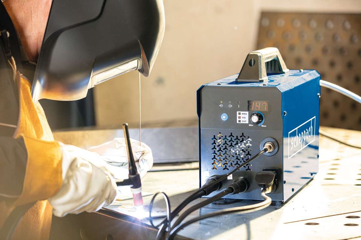 Ein Arbeiter verwendet das 3in1 Kombi-Schweißgerät WSE4000-CUT von Scheppach. Der Arbeiter trägt eine Schweißerhaube und Handschuhe und hält einen Schweißbrenner in der Hand. Das Gerät zeigt eine Temperatur von 147 an.