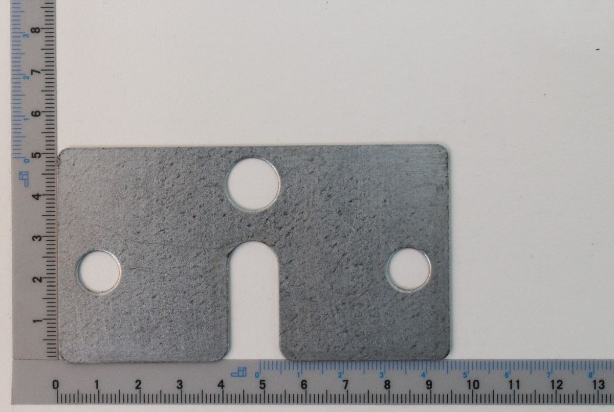 Ein Ausgleichsblech mit drei Löchern, von vorne fotografiert. Das Blech ist 94 mm breit und 52 mm hoch.