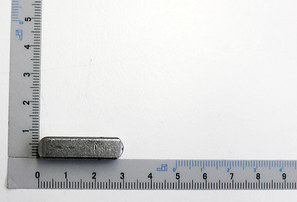 Eine Passfeder neben einem Lineal zur Größenveranschaulichung. Die Passfeder ist von vorne zu sehen.