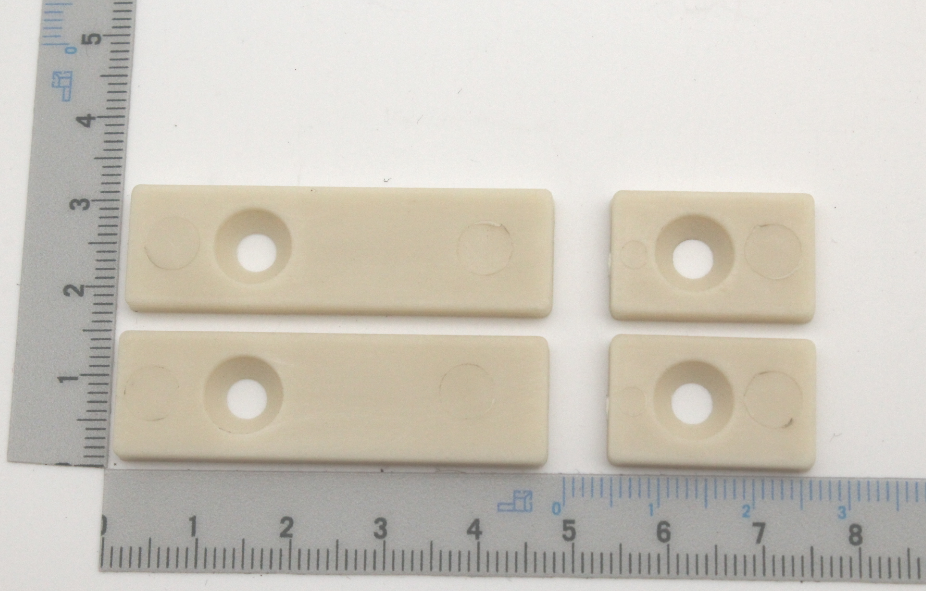 Ein Satz Führungsschienen mit vier Teilen, jeweils mit zwei Löchern. Die Teile sind etwa 5 cm lang und 2 cm breit. Die Schienen sind neben einem Lineal mit Zentimeter- und Millimeterskala platziert.