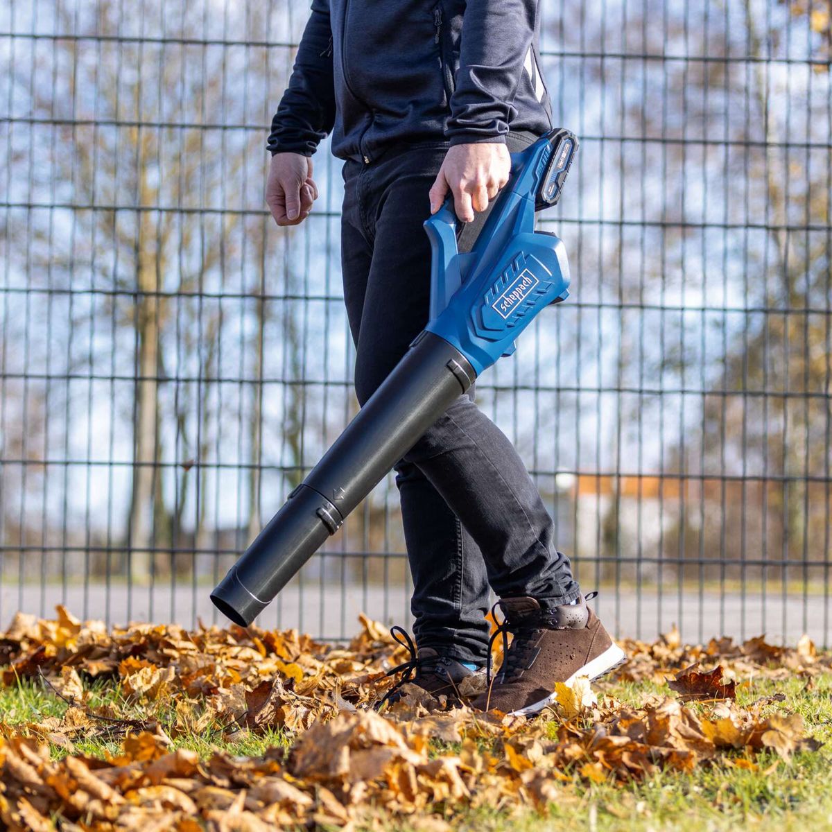 Person beim Einsatz eines Scheppach-Akku-Laubbläsers mit Akku und Ladegerät