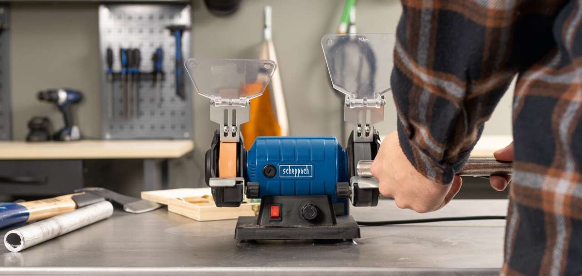 Doppelschleifer HG35 von Scheppach im Einsatz. Ein Benutzer bearbeitet ein Werkstück mit der Schleifscheibe. Im Hintergrund sind Werkzeuge und eine Werkbank zu sehen.