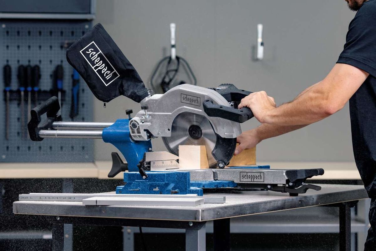 Kappzugsäge HM110MP von Scheppach im Einsatz. Ein Benutzer bedient die Säge an einem Werkstück. Die Säge ist auf einem Tisch montiert und wird von einem Benutzer mit beiden Händen gehalten.