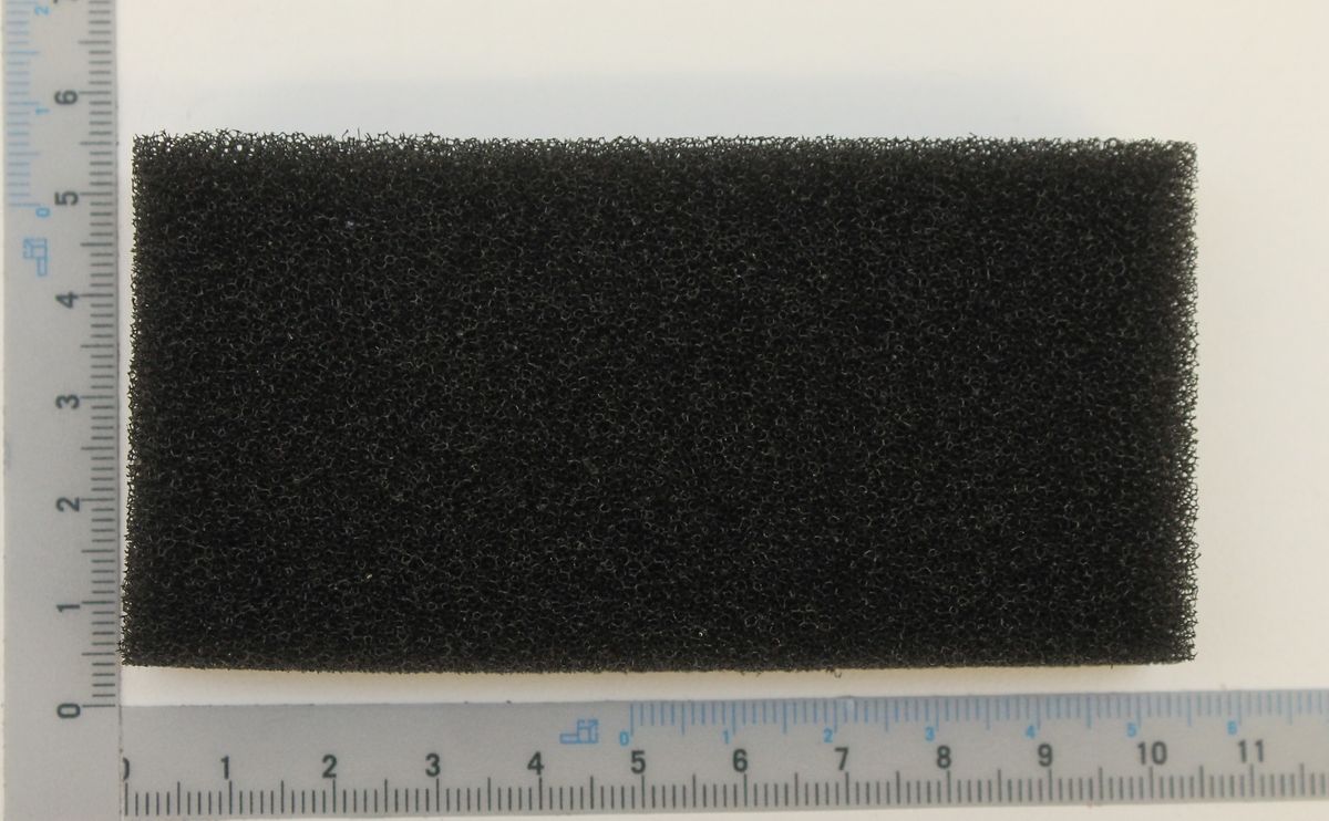 Ein schwarzer Schwammfilter vor einem Lineal. Der Filter ist etwa 10 cm breit und 6 cm hoch.