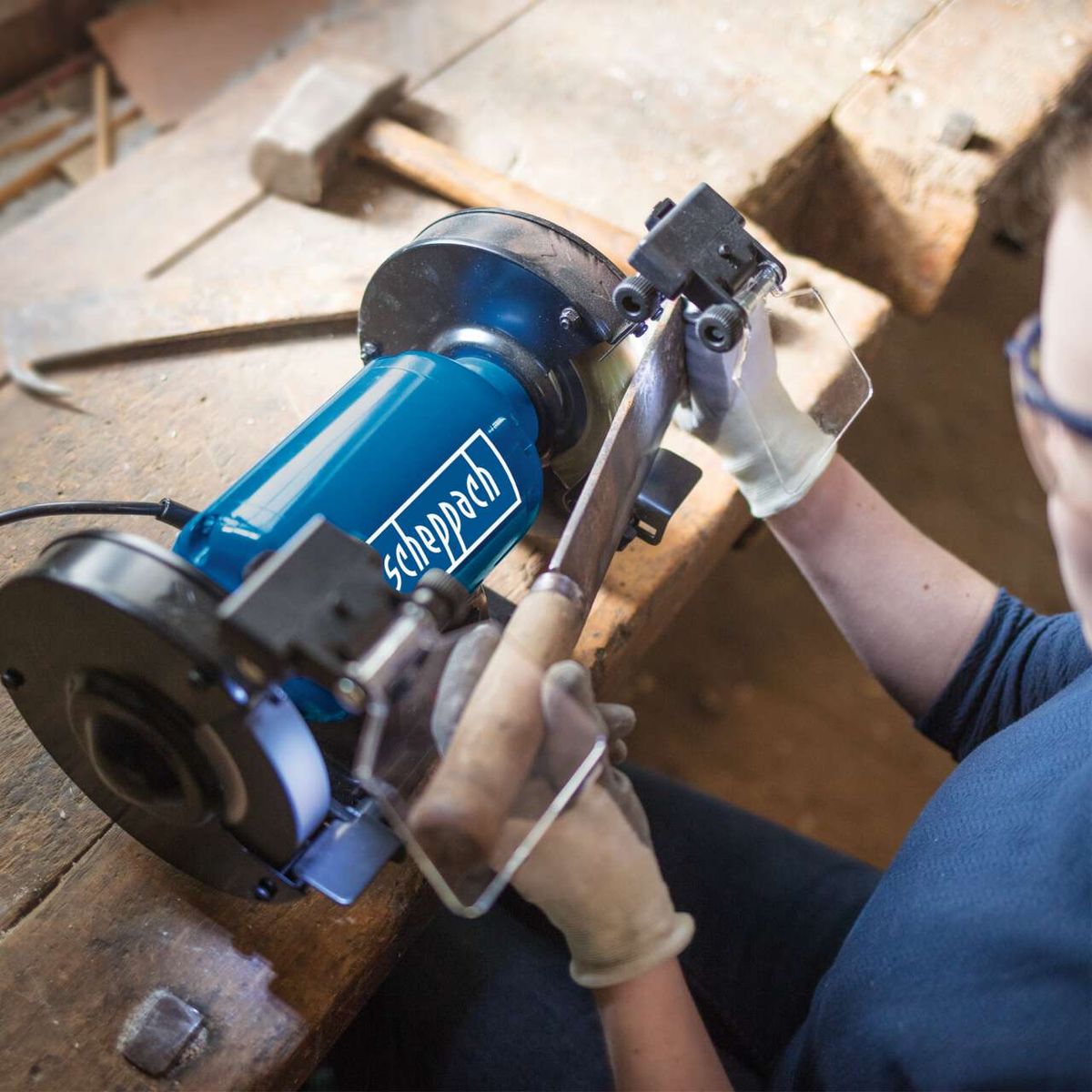 Der Scheppach Doppelschleifer SM150L mit 150mm Schleifteller und Schutzabdeckung. Die Handgriffe sind verstellbar und ermöglichen eine präzise Kontrolle während der Arbeit.