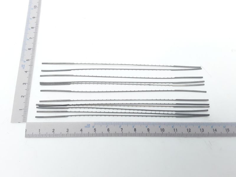 Ein Satz von zwölf Laubsägeblättern, jeweils 130 mm lang, mit feinen Zähnen. Die Blätter sind nebeneinander auf einem Lineal ausgelegt, das die Länge der Blätter misst.