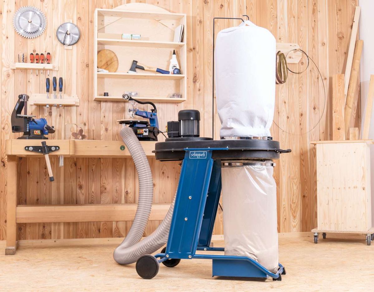 Absauganlage HD12 Scheppach mit Auffangbehälter und Schlauch, Werkbank mit Werkzeugen im Hintergrund.
