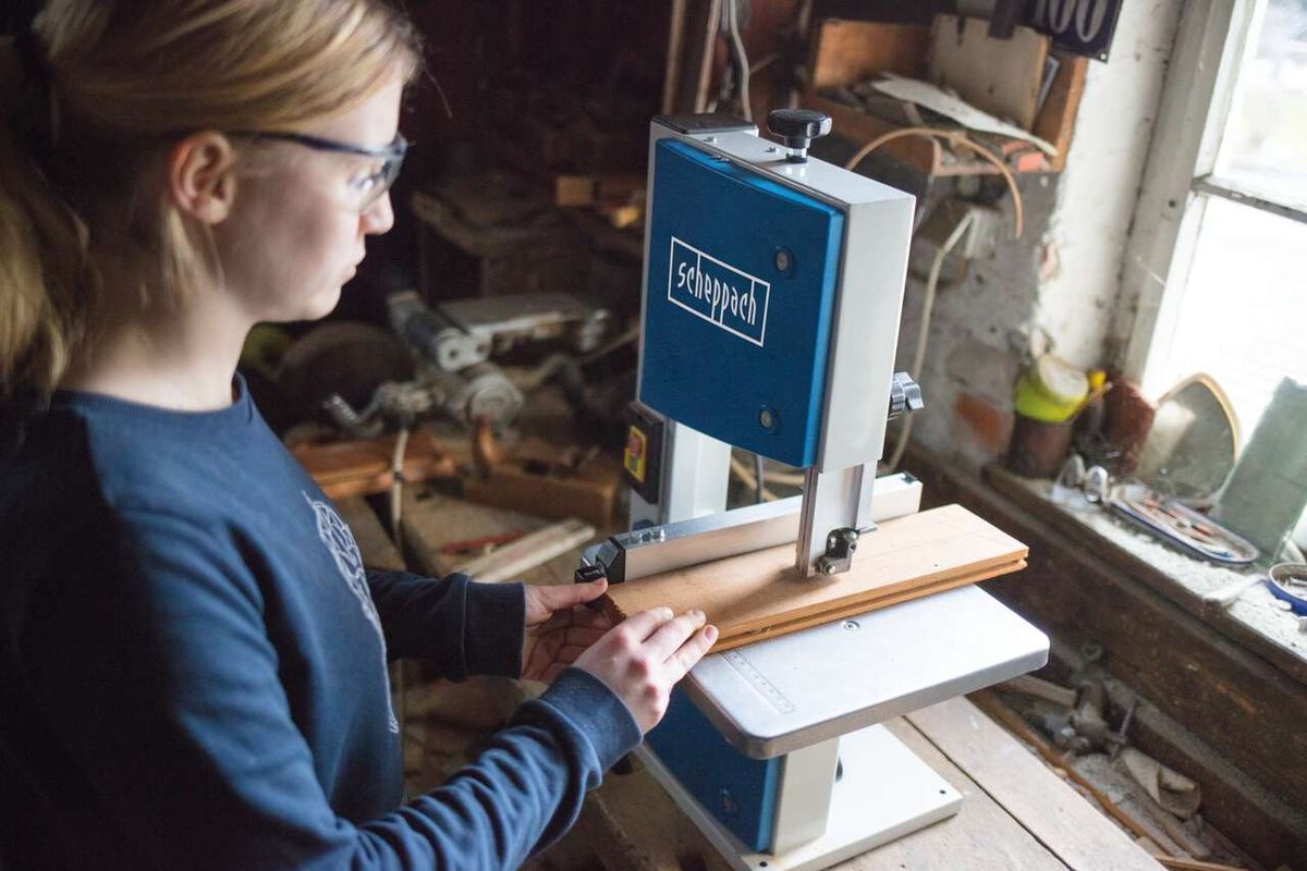 Eine Person bedient eine Bandsäge HBS20 von Scheppach. Die Maschine ist in Betrieb und schneidet Holz. Die Person trägt Schutzbrille und arbeitet konzentriert.