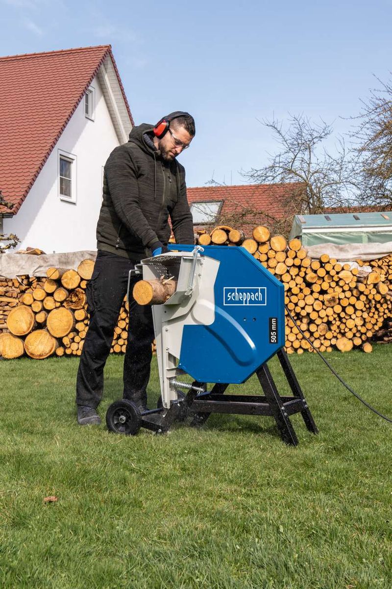 Ein Mann bedient die Wippsäge HS510 von Scheppach im Freien. Im Hintergrund sind Holzstapel zu sehen.