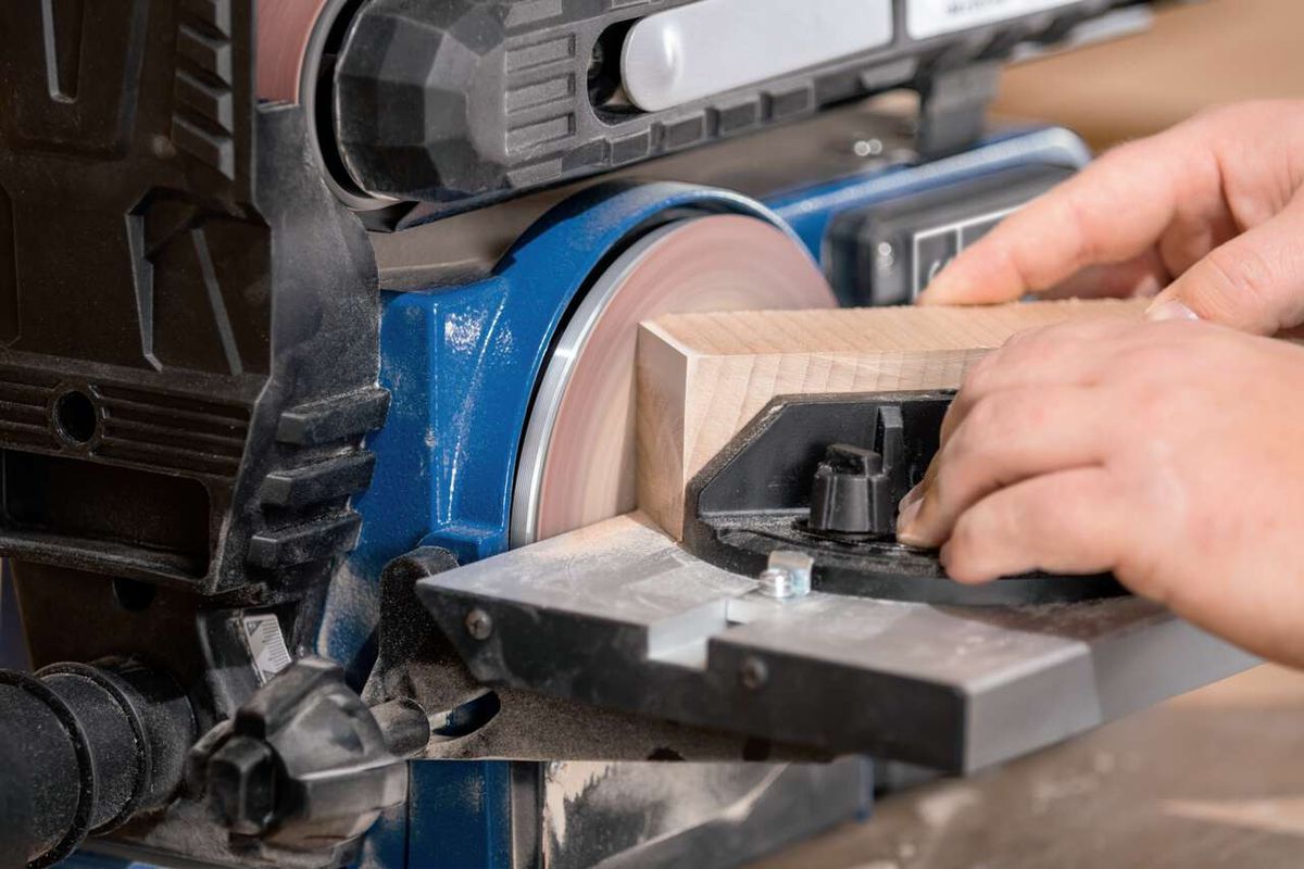 Band- und Tellerschleifer BTS900 von Scheppach. Ein Holzstück wird mit der Hand geführt und geschliffen.