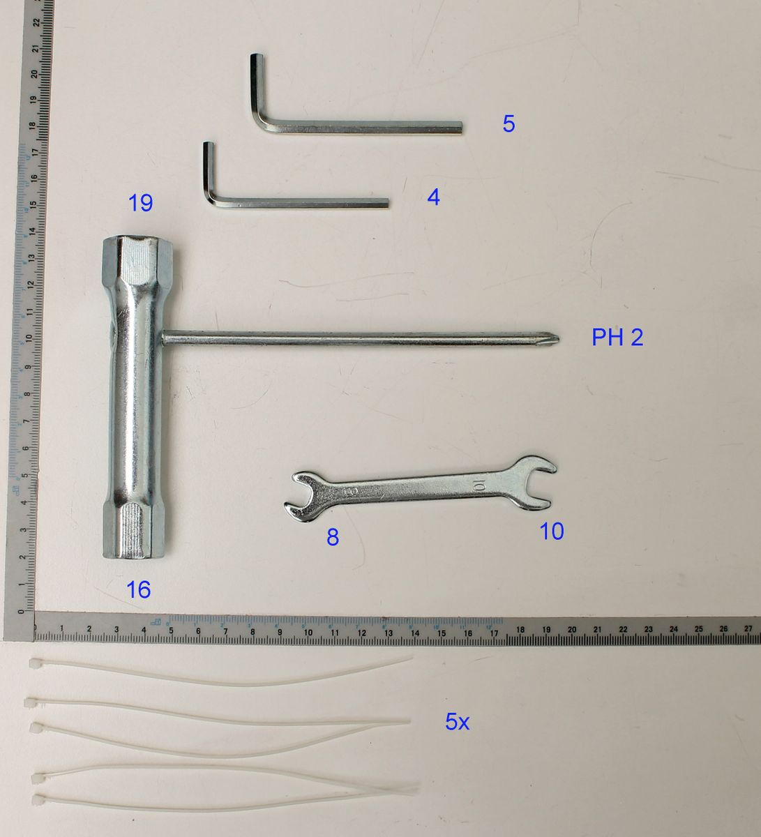 Ein grauer Metallstab mit einem L-förmigen Ende, daneben ein Lineal zur Größenmessung. Teil des Beipackbeutels 5910702019 von Scheppach.