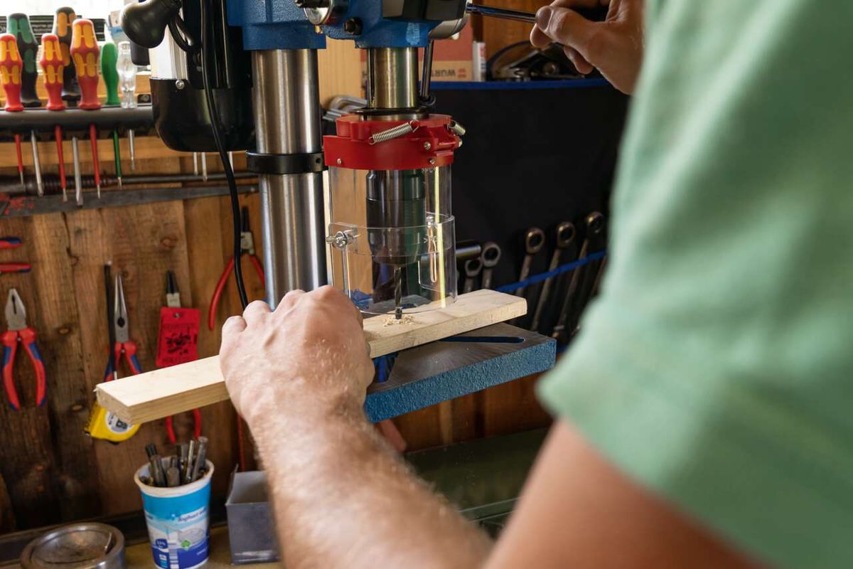 The Scheppach bench drill DP19Vario in use. A wooden board is clamped on the worktable and being drilled.