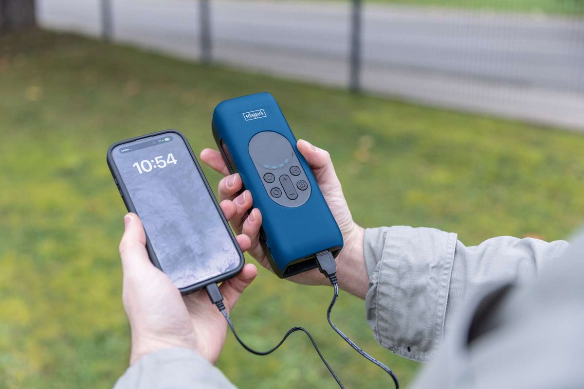 Hände halten ein Smartphone und ein Scheppach-Ladegerät. Das Smartphone zeigt 10:54 Uhr an und ist mit dem Ladegerät verbunden.