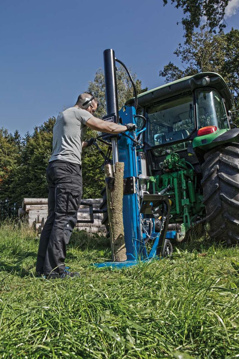 Ein Mann bedient einen Holzspalter HL3000GM von Scheppach. Der Holzspalter ist an einen Traktor angeschlossen und wird auf einer Wiese verwendet.
