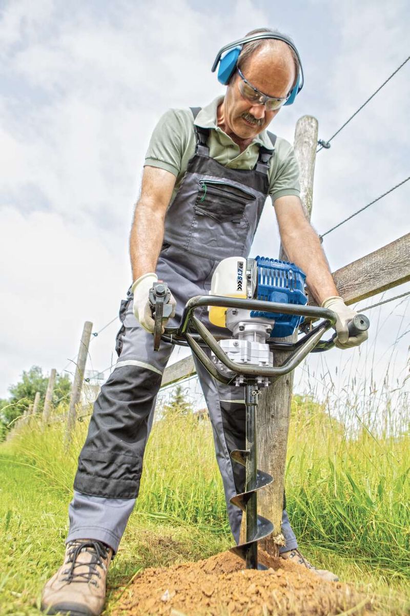 Ein Arbeiter verwendet den Benzin Erdbohrer EB1700 von Scheppach zum Bohren in den Boden. Der Arbeiter trägt Schutzausrüstung und hält den Bohrer mit beiden Händen. Der Bohrer hat eine Bohrlänge von 800mm und ist inkl. Bohrerset.