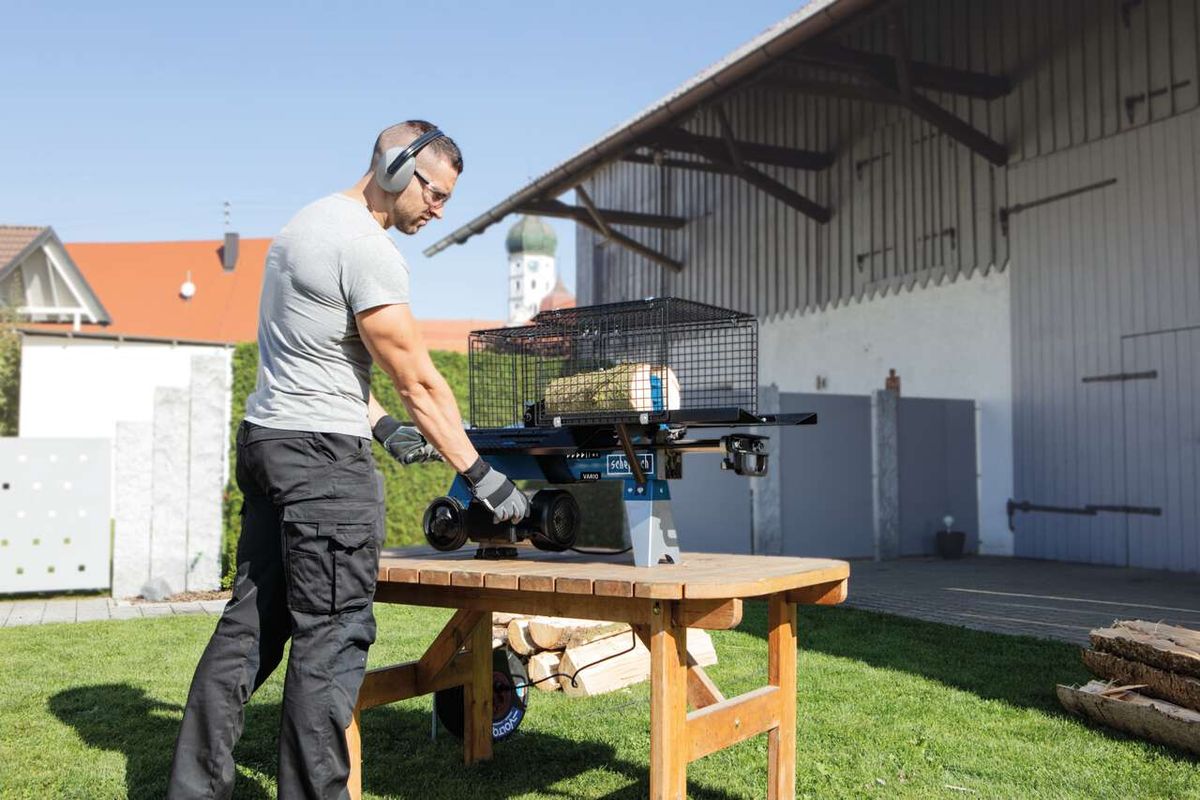 Man operating a Scheppach HL460 horizontal log splitter with a basket for split wood