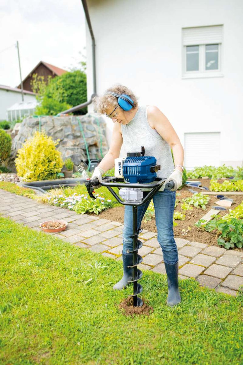Frau nutzt Scheppach-Erdbohrer für Gartenarbeit, Bohrgerät mit Bohraufsatz im Einsatz