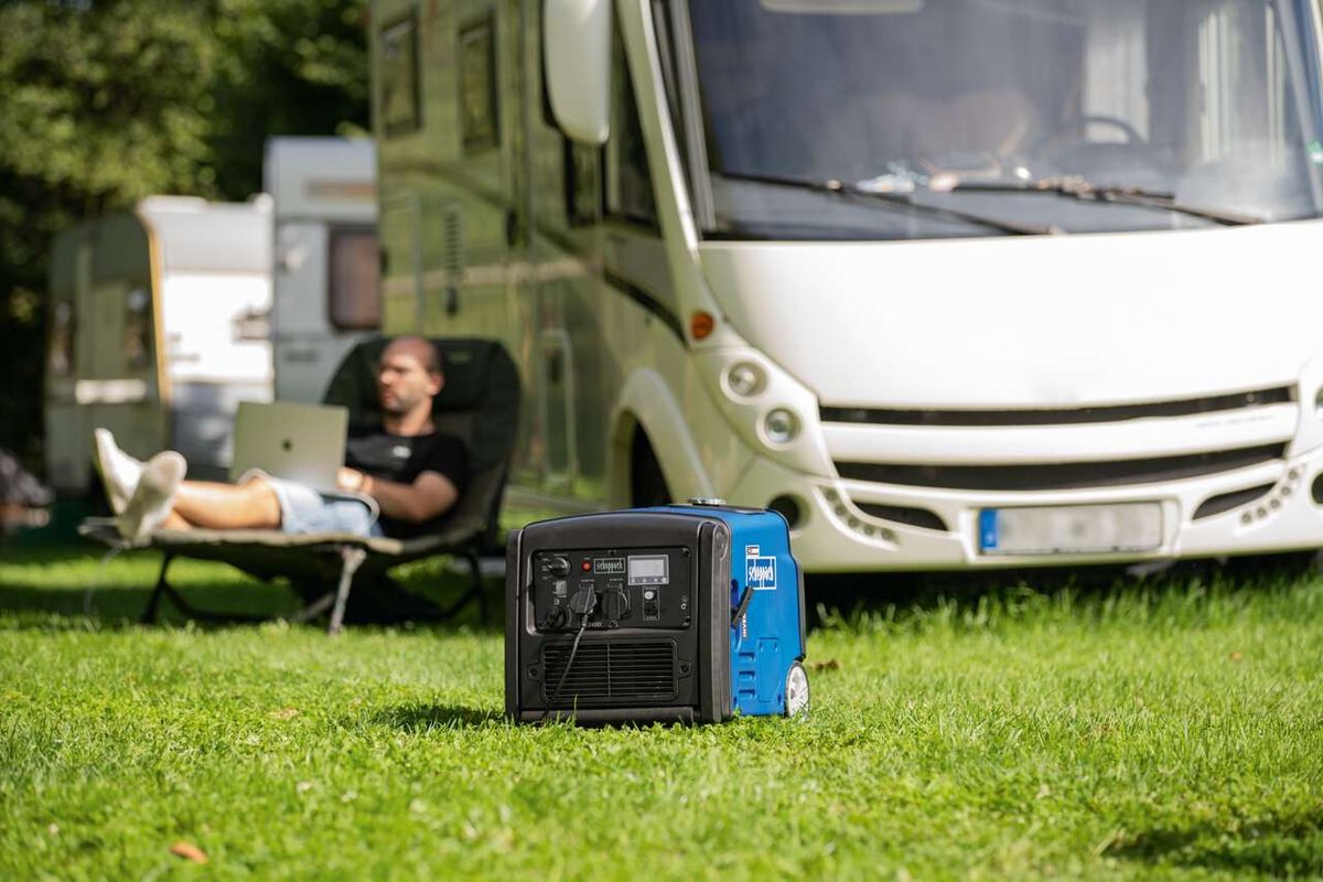 Ein Mann sitzt vor einem Wohnmobil und arbeitet auf einem Laptop. Vor ihm steht ein Scheppach Inverter SG3400i auf dem Rasen.