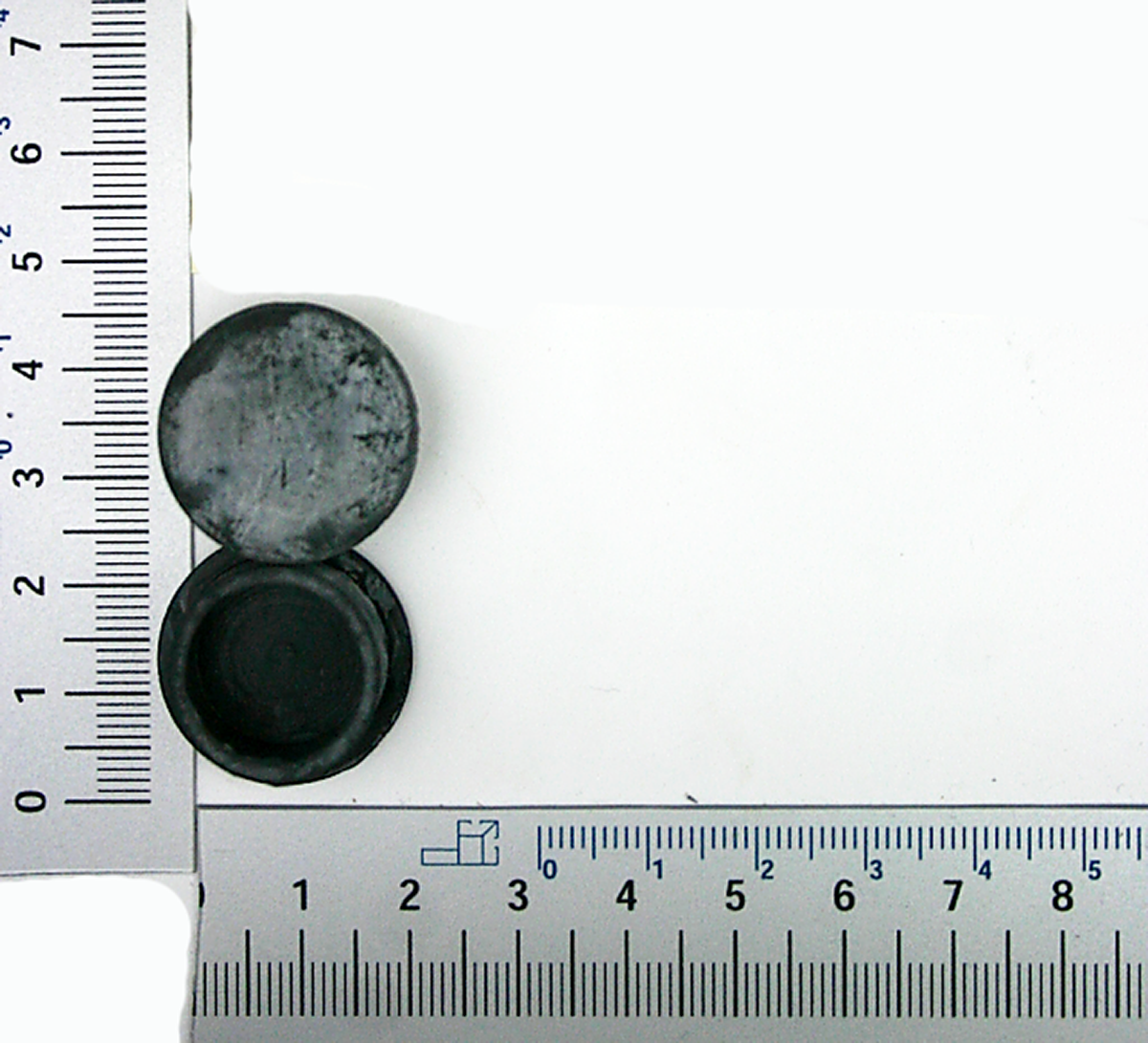 Ein Stopfen neben einem Lineal zur Größenveranschaulichung. Der Stopfen ist rund und hat einen Durchmesser von etwa 2,5 Zentimetern.